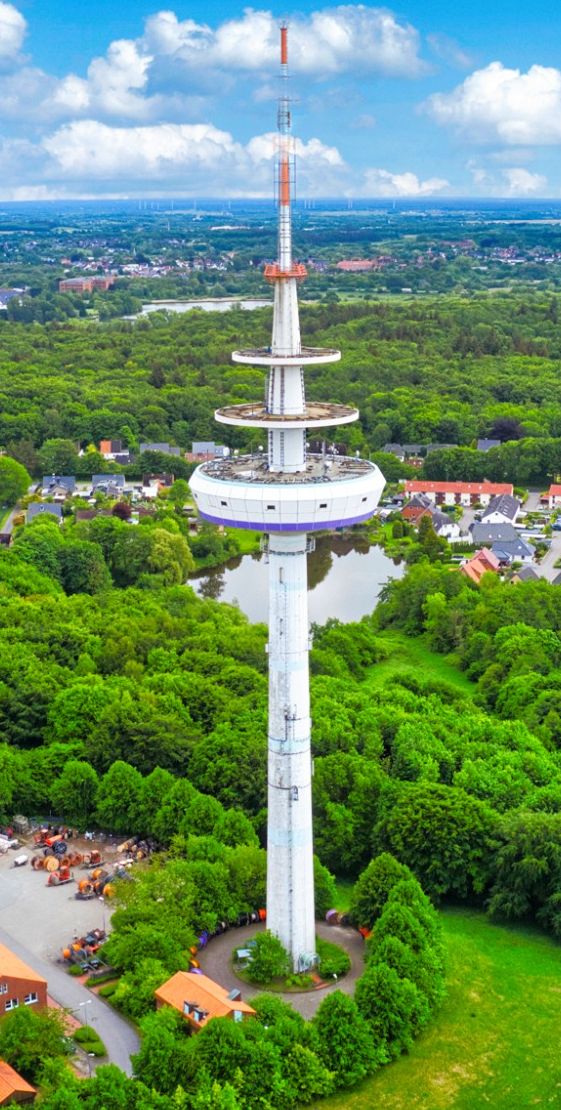ein großer Fernsehturm vor blauem Himmel und grüner Landschaft aus Drohnenperspektive